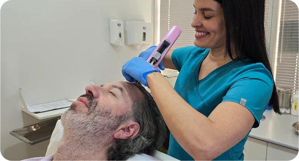 Profesional aplicando un tratamiento anticaída en el cuero cabelludo de un paciente en consulta.